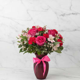 Pink and red flower arrangement in a burgundy vase with a pink ribbon