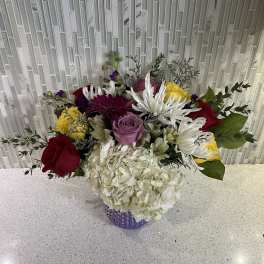 Mixed bouquet in a purple vase with roses, hydrangea, and white daisies