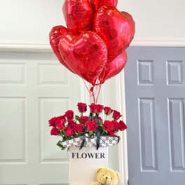 Red roses in a gift box with heart-shaped balloons and a teddy bear