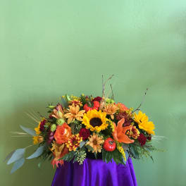 Autumn floral arrangement with sunflowers, lilies, and roses on a purple drape