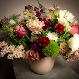 Mixed bouquet of roses, ranunculus, and stock in a beige vase