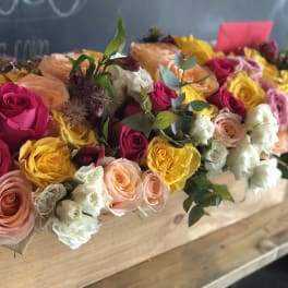Long box arrangement of roses in pink, yellow, peach, and white