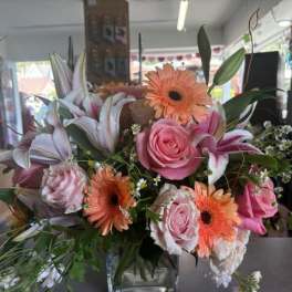 Bouquet of pink roses, lilies, and orange gerbera daisies in a glass vase