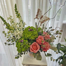 Pink roses and green hydrangeas in a white vase with a butterfly accent
