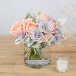 Pastel rose bouquet in a clear glass vase beside a white candle