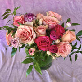 Pink and peach roses in a glass vase with purple flowers