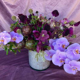 Purple floral arrangement with orchids in a white vase