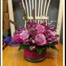 Pink roses and purple flowers arranged in a round glass vase