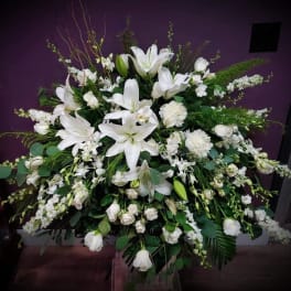 Large all-white floral arrangement with lilies, roses, and other blooms in a fan shape.