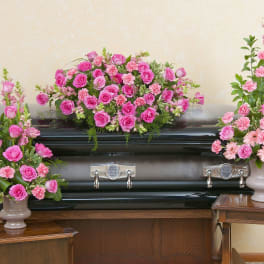 Pink rose and carnation casket spray with two matching standing arrangements on a dark casket