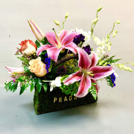 Pink lilies and roses arranged in a moss-covered Prada box