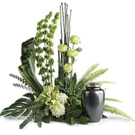 Green and white floral cremation arrangement surrounding a black urn with tall accents