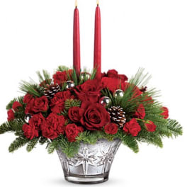 Red roses and pine in a clear glass vase with two red taper candles