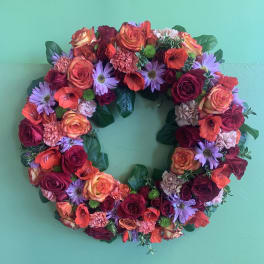 Circular floral wreath with roses, daisies, and carnations on a green background