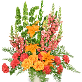 Orange lilies and roses with pink snapdragons in a white container