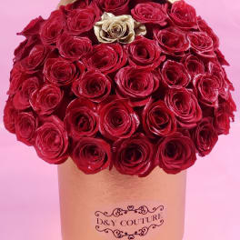 Red roses arranged in a gold round box with one gold rose