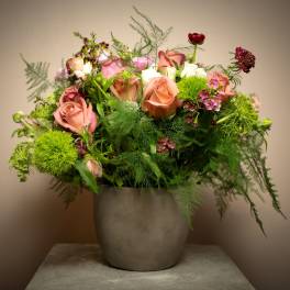 Lush peach rose and mixed flower arrangement with airy greenery in a gray ceramic pot