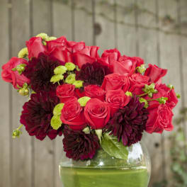 Red roses and dark burgundy blooms in a round glass vase