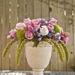 Pink and lavender roses arranged in a white pedestal vase