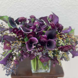 Purple calla lilies and roses arranged in a clear square vase