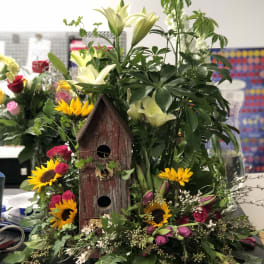 Mixed bouquet with lilies, sunflowers, and roses around a wooden birdhouse