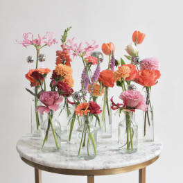 Small floral stems in clear glass bottles on a round table
