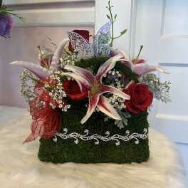 Red roses and pink lilies in a moss-covered box with a butterfly decoration