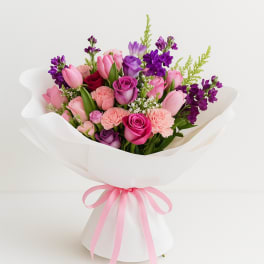 Pink and purple mixed bouquet wrapped in white paper with a pink ribbon