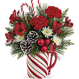 Holiday bouquet in a candy cane mug with red flowers and pinecones