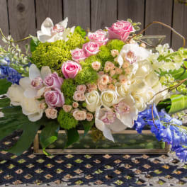 Mixed floral arrangement in a rectangular glass vase with pink, white, and blue blooms