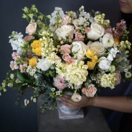 Large bouquet of white, pink, and yellow flowers held by a person