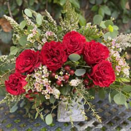 Red roses arranged with pink filler flowers in a square vase