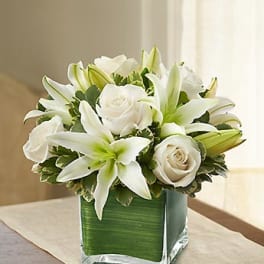 White lilies and roses arranged in a square glass vase