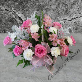 Pink roses and white carnations arranged in a basket with a pink ribbon