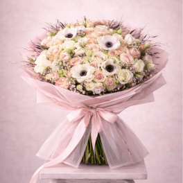 Large pastel bouquet of roses and white anemones wrapped in pink paper