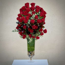 Tall arrangement of abundant red roses in a clear glass vase with stones at the base