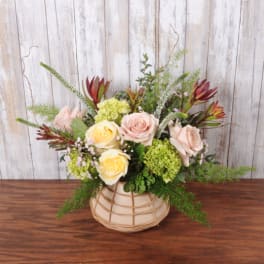 Low peach and yellow rose arrangement with green accents in a round basket vase