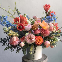 Mixed bouquet of coral, pink, blue, and white flowers in a white vase