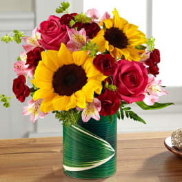 Bouquet of sunflowers, pink roses, and red carnations in a green vase