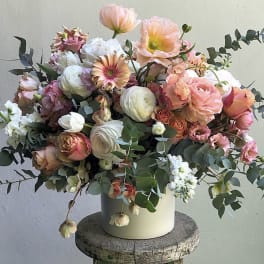 Mixed bouquet of peach, pink, and white flowers in a white vase