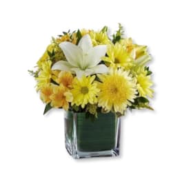 Yellow flowers with a white lily in a square glass vase