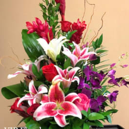 Tall floral arrangement with pink lilies, red roses, and purple orchids in a white container