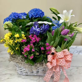 Basket arrangement with blue hydrangeas, yellow daffodils, pink flowers, and white lilies