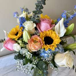 Bouquet of roses, sunflowers, lilies, and blue flowers in a glass vase