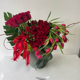 Red roses and pink tulips arranged in a ribbed vase with a red ribbon