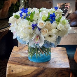 White floral arrangement with blue accents in a clear glass vase