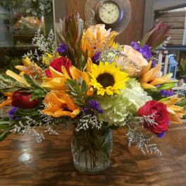Mixed bouquet with sunflower, orange lilies, red roses, and hydrangea in a clear glass vase