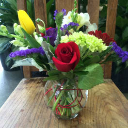 Mixed bouquet with a red rose, yellow tulip, and white calla lilies in a glass vase