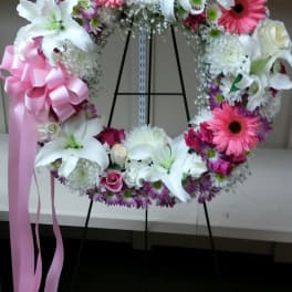 Floral wreath with white lilies, pink gerberas, and a pink ribbon bow