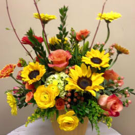 Bright mixed bouquet in a tan vase with sunflowers and roses
